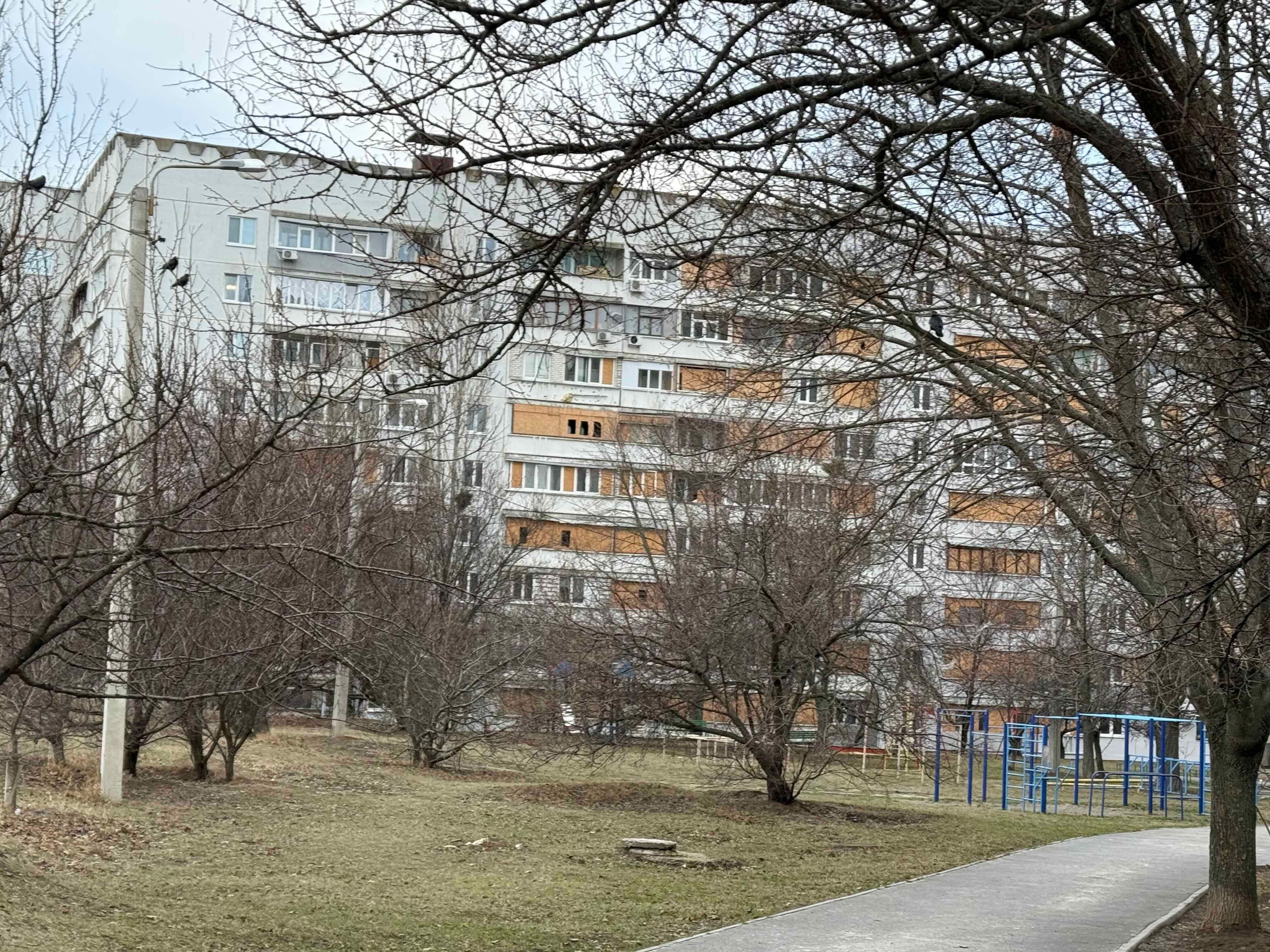 Улица Натальи Ужвий. В доме видны отверстия, прорезанные в закрывающей выбитое окно фанере. Фото: ЦЗПЧ «Мемориал»